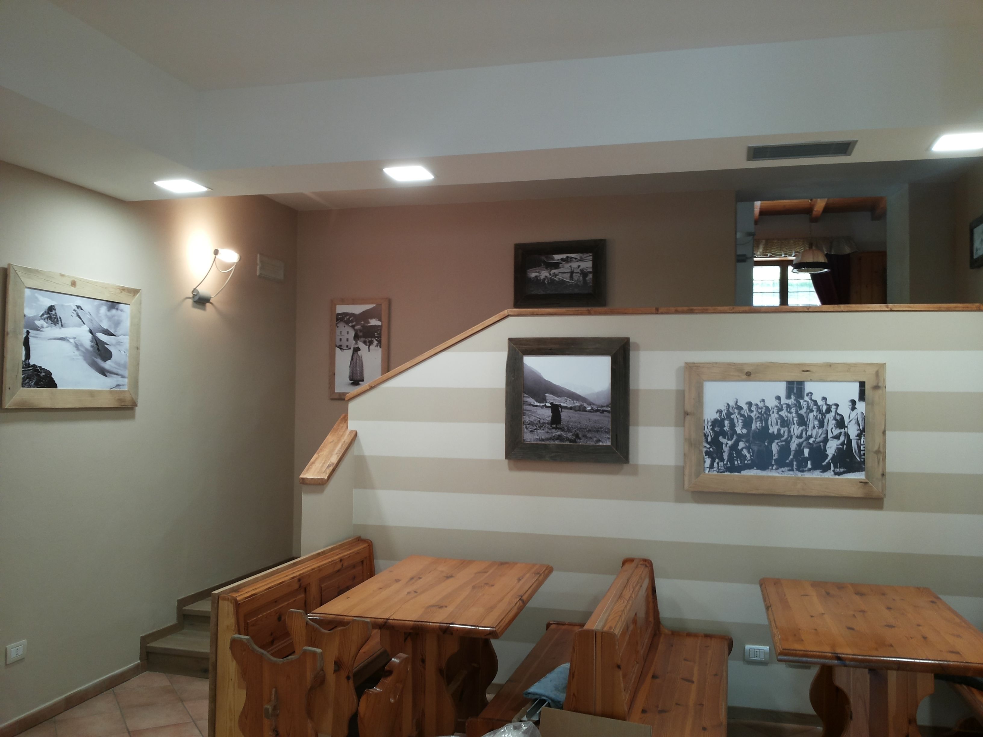 Une pièce avec des bancs et des tables en bois, un escalier et plusieurs photographies encadrées accrochées aux murs.