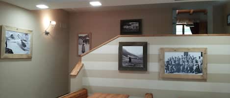Une pièce avec des bancs et des tables en bois, un escalier et plusieurs photographies encadrées accrochées aux murs.