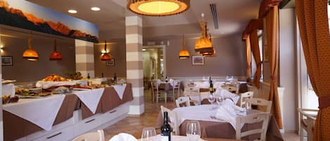 A restaurant with white tablecloths, wine glasses, and a bottle of wine on the tables.