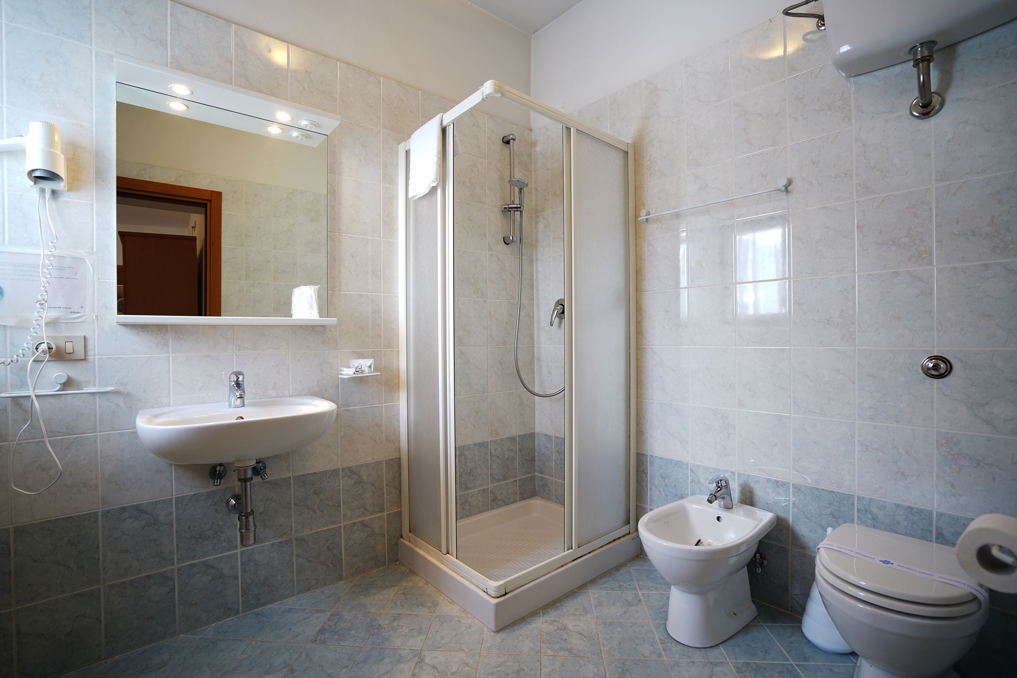 A bathroom with a glass-enclosed shower, a sink, a bidet, and a toilet.