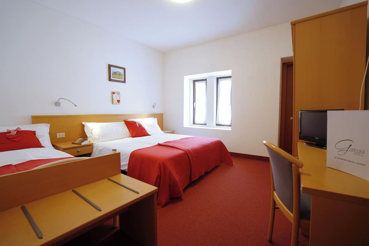 Een hotelkamer met twee bedden, een bureau, een stoel, een televisie en een raam.