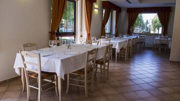 A dining area with multiple tables and chairs, large windows with curtains, and a tiled floor.