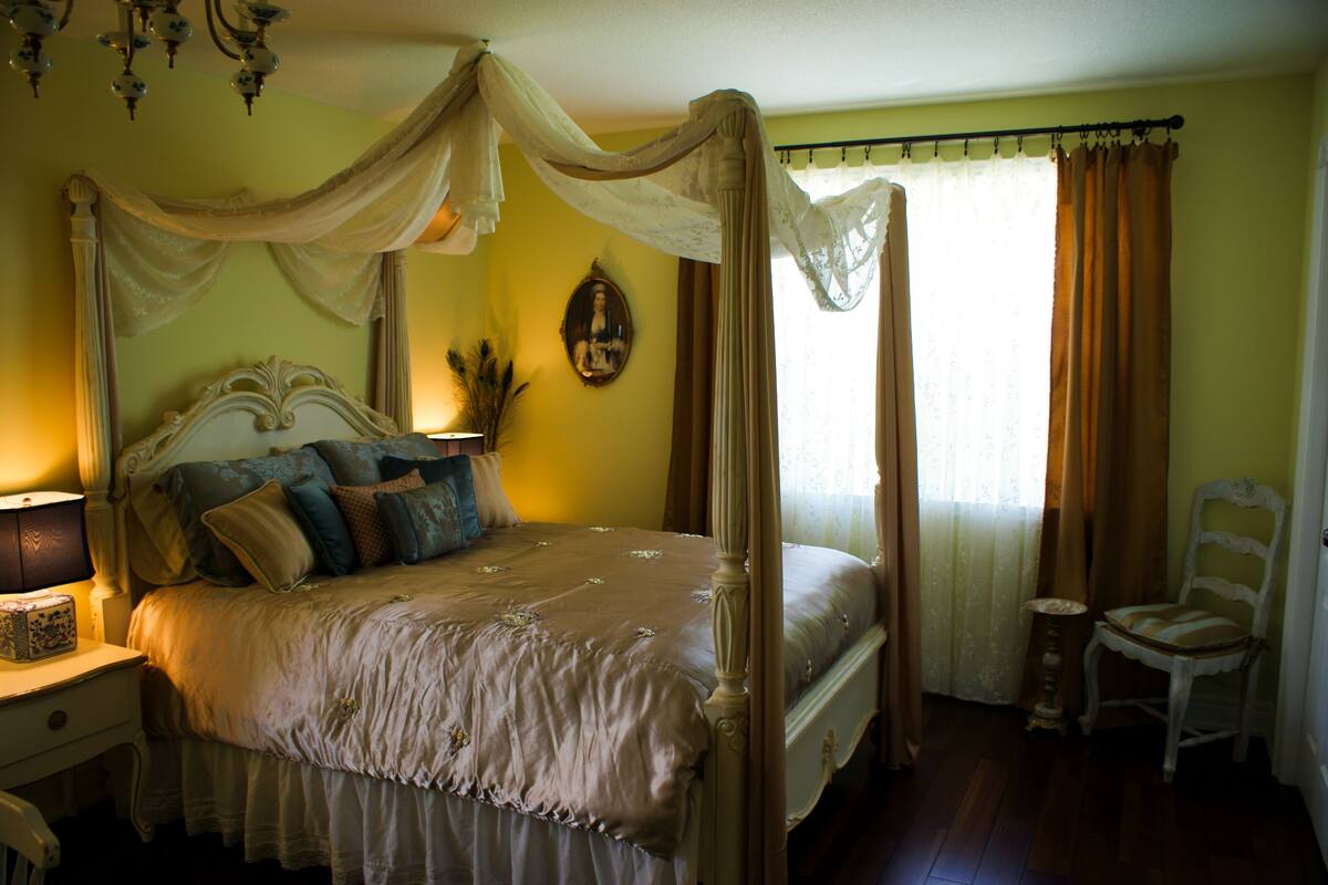 A four-poster canopy bed with a nightstand, a chair, and a mirror on the wall.