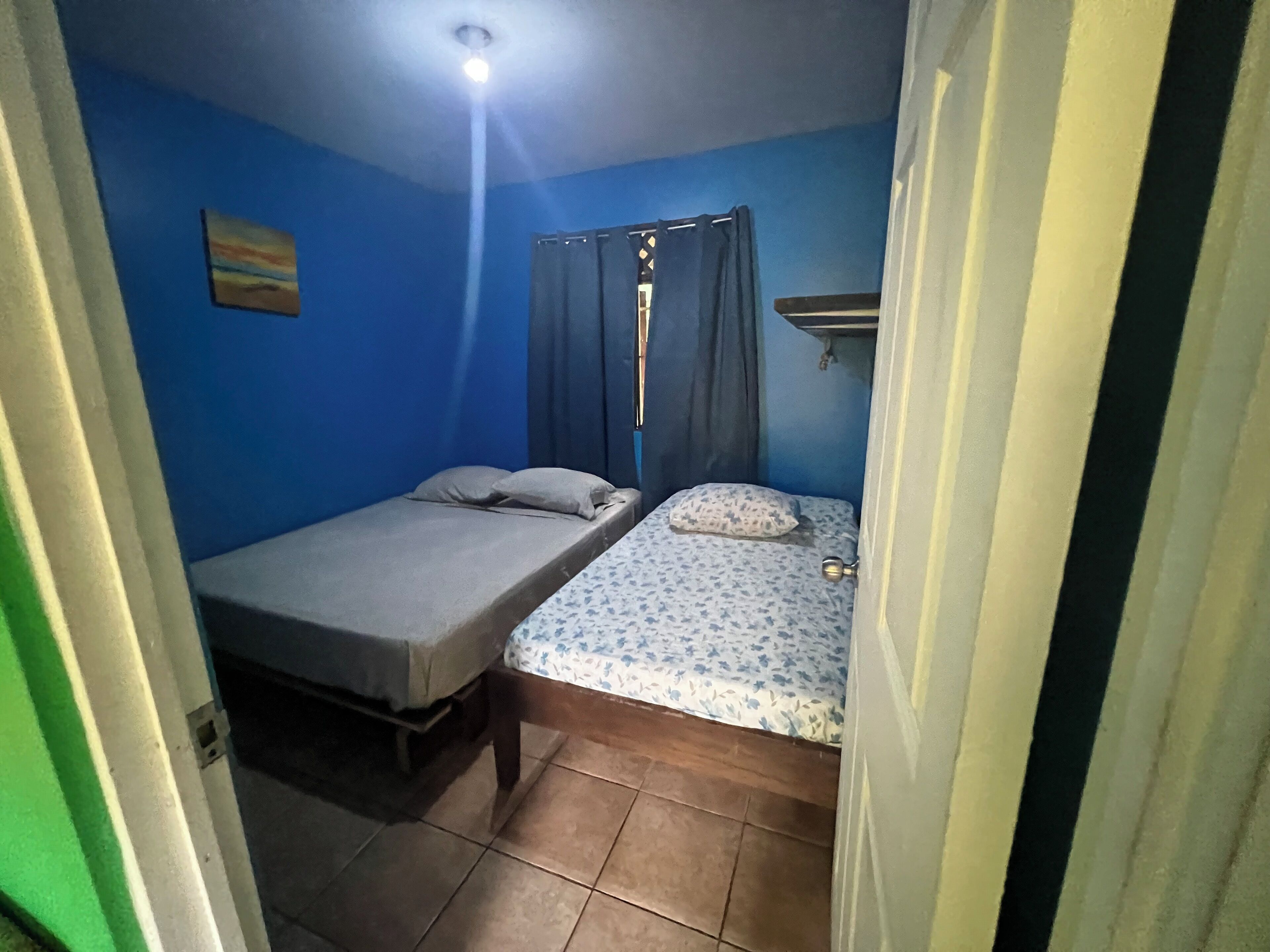 Une petite pièce avec deux lits, un luminaire au plafond et une étagère fixée au mur.