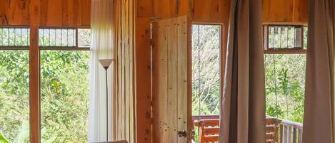 A wooden cabin with a bed, a table with chairs, and a view of greenery outside.