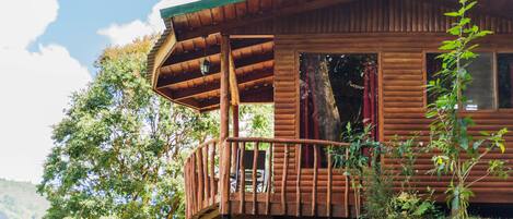 A wooden cabin with a balcony, surrounded by lush greenery and trees.