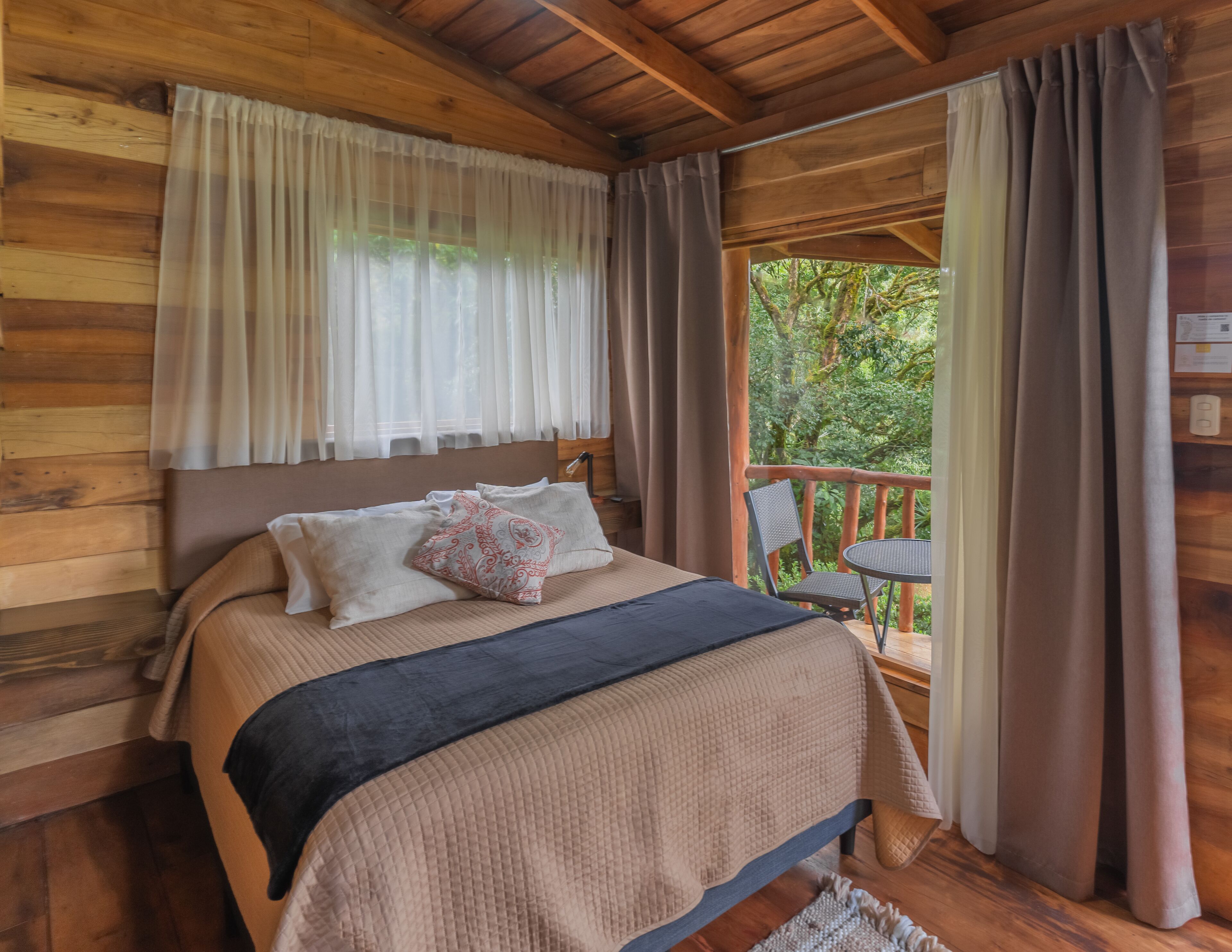 Un dormitorio de cabaña de madera con una cama, una mesita de noche y vistas al exterior.