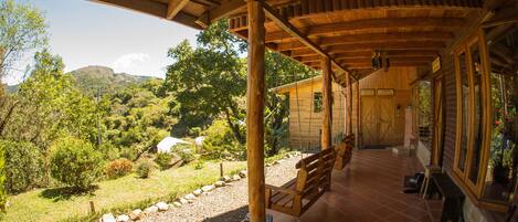A wooden porch with a bench, a view of a landscaped garden, and a mountain in the background.