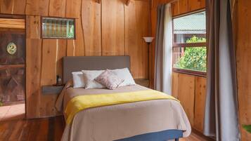 Ein Schlafzimmer einer Holzhütte mit einem Bett, einem Nachttisch, einem Fenster mit Vorhängen und einer Tür mit einer Nummer.