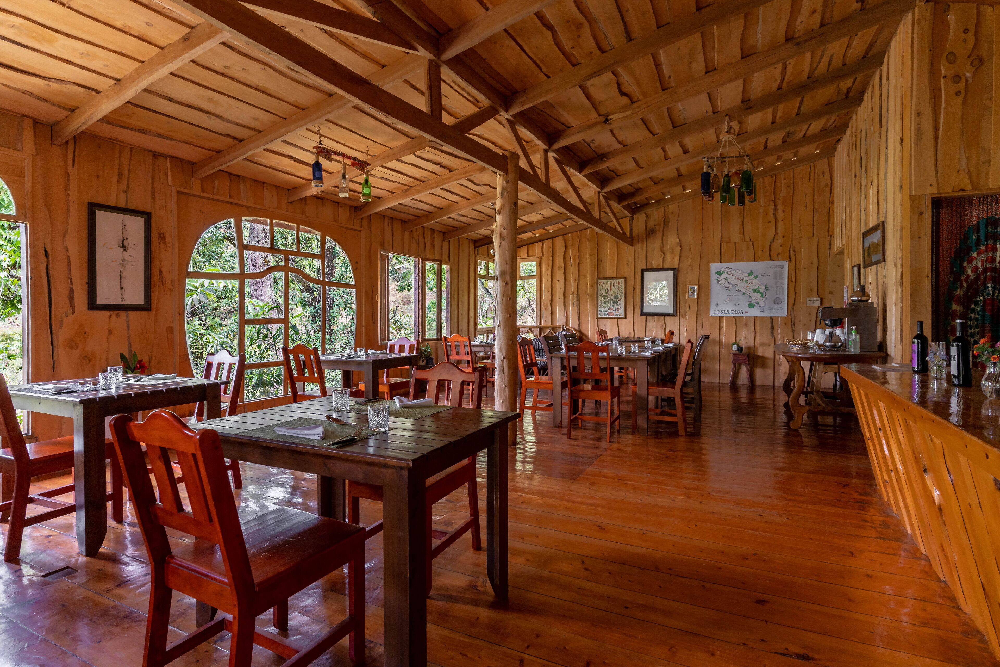 A wooden interior with tables and chairs, large windows, and a map on the wall.
