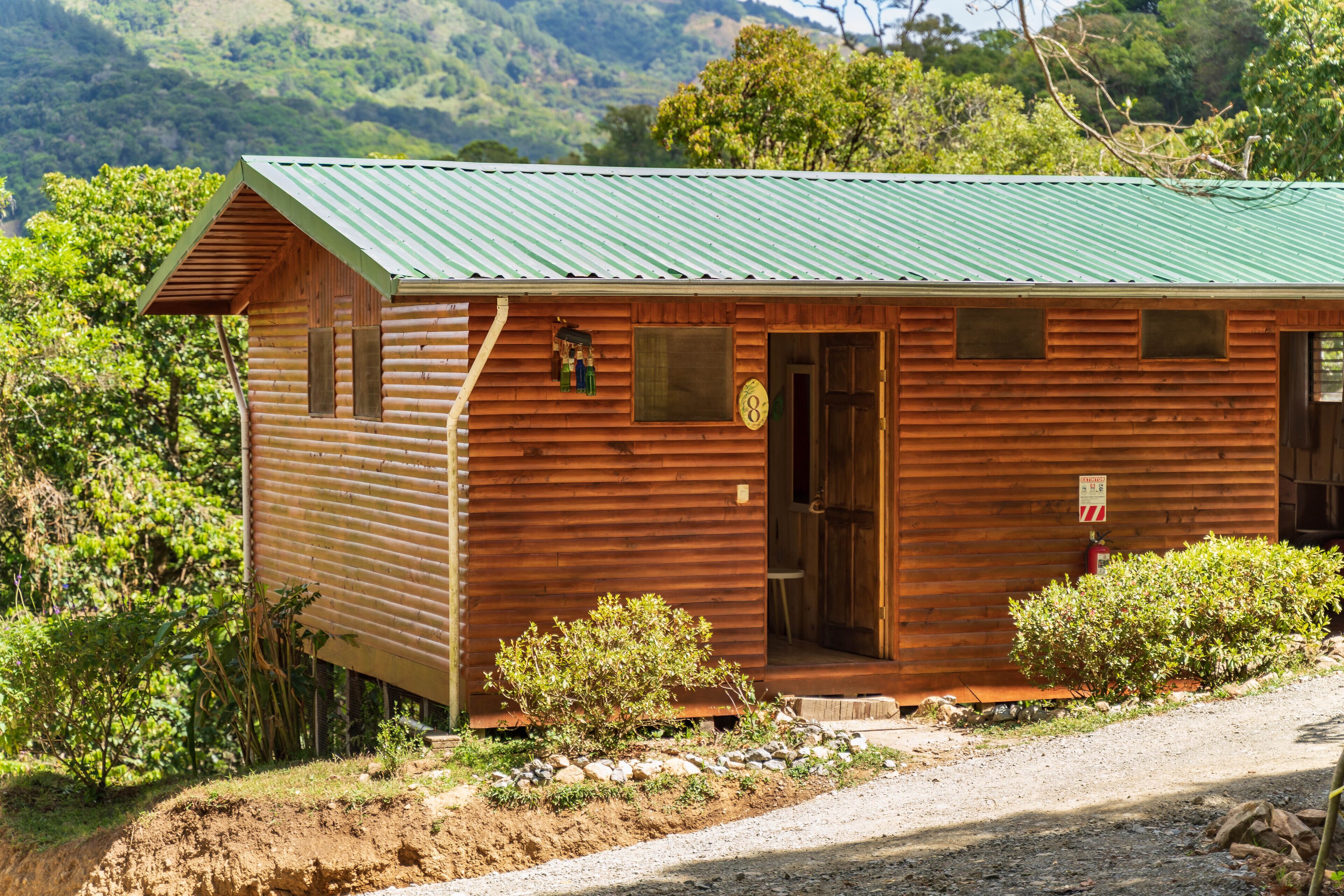 Una cabaña de madera con techo verde, una puerta y un ventanal pequeño.