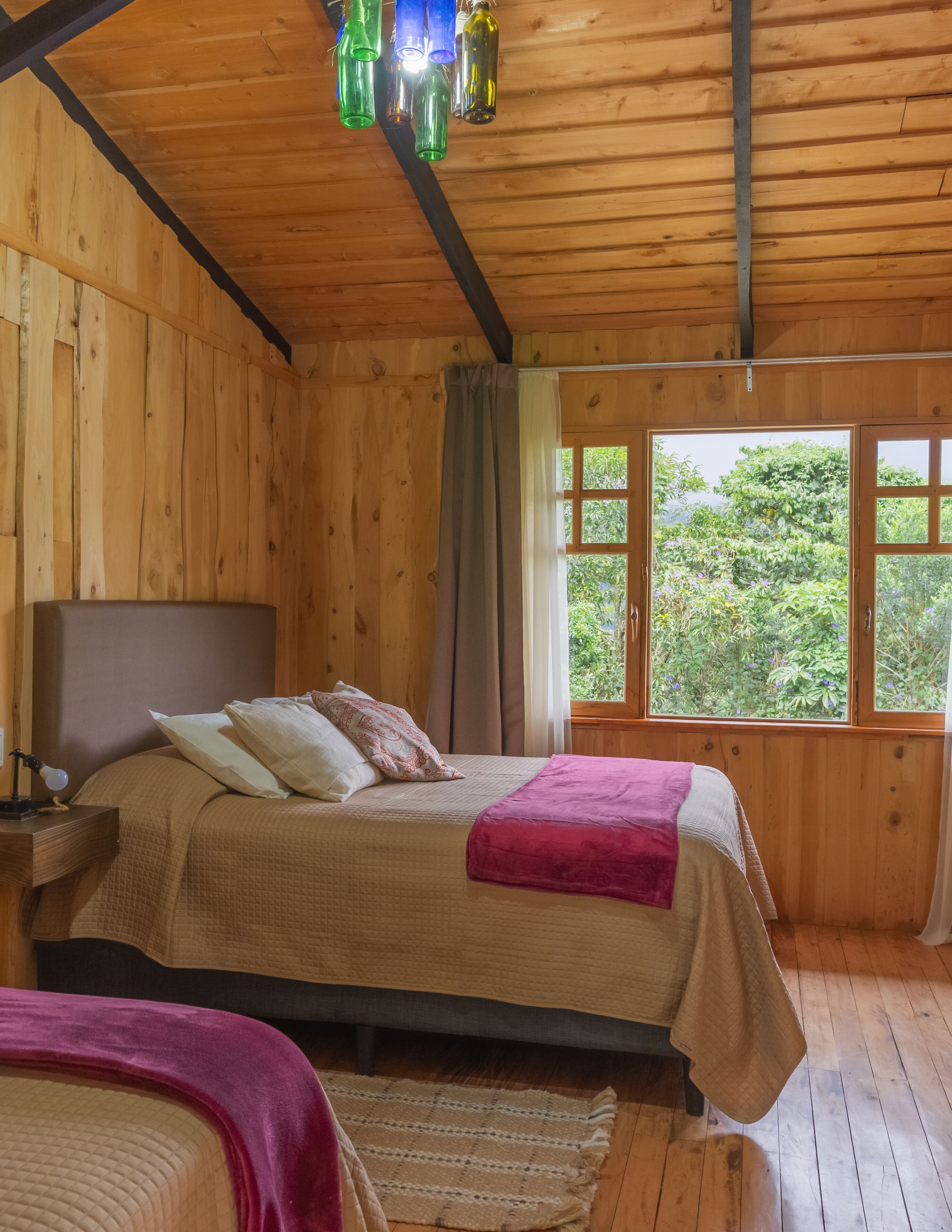 A wooden cabin bedroom with a bed, bedside table, and curtains.
