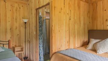 Een slaapkamer in een houten hutje met twee bedden, een nachtkastje, een lamp en een deur naar een badkamer.