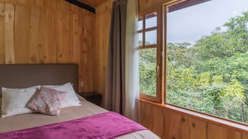 A wooden room with a bed, a nightstand, and a window with a view of greenery.