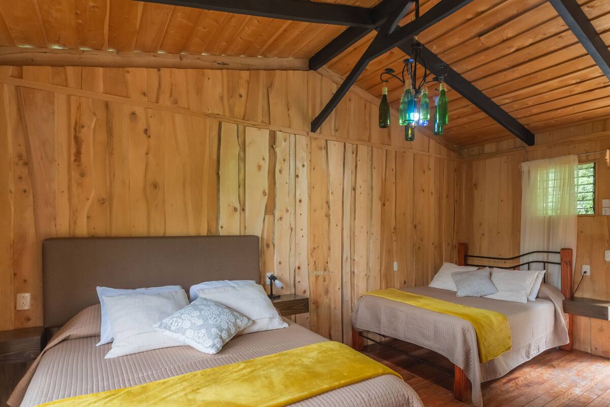 A wooden cabin room with two beds, each with a yellow blanket, wooden walls, and a ceiling with exposed beams.