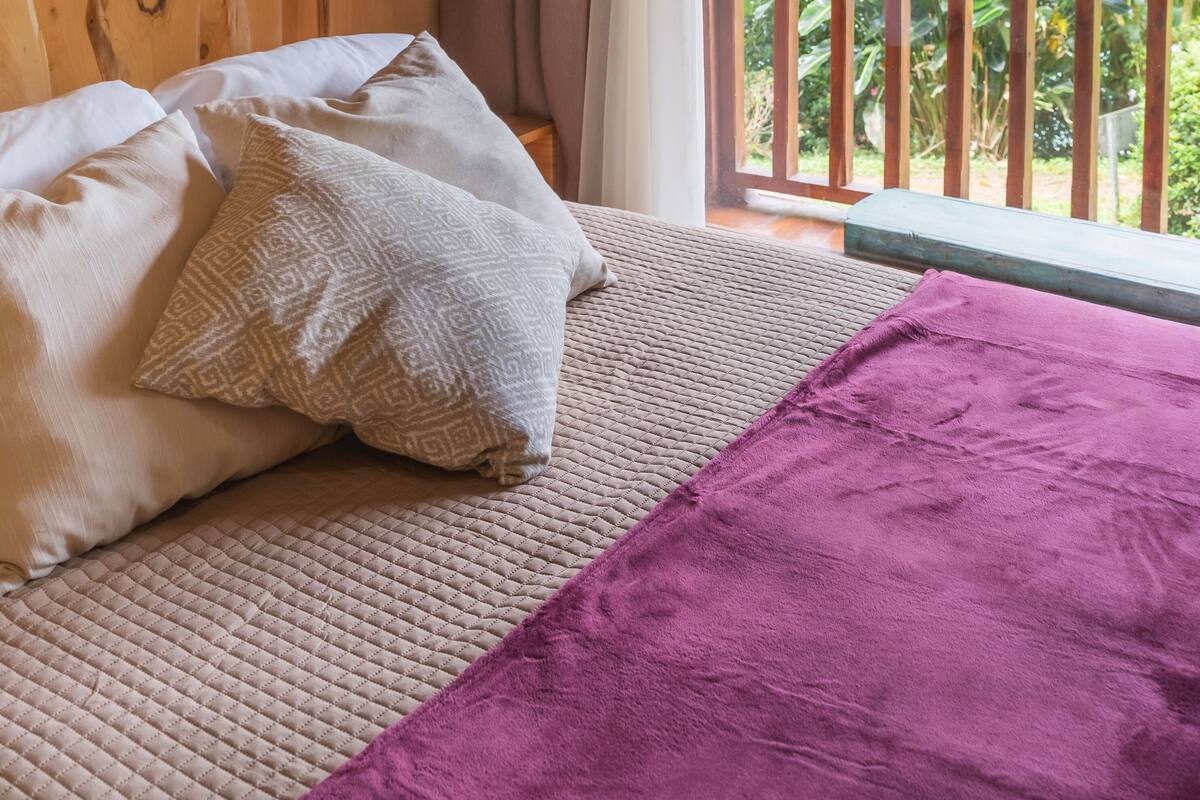 A wooden cabin room with a bed, pillows, and a purple blanket.