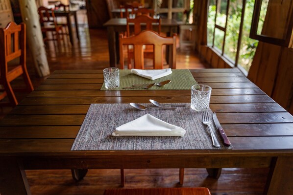 A wooden dining table with a placemat, cutlery, and glasses set for two. - Cedrela Ecolodge (Copey)