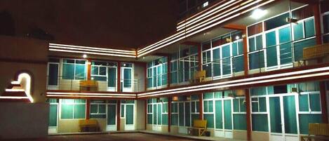 A multi-story hotel with a central courtyard, balconies, and a neon sign.