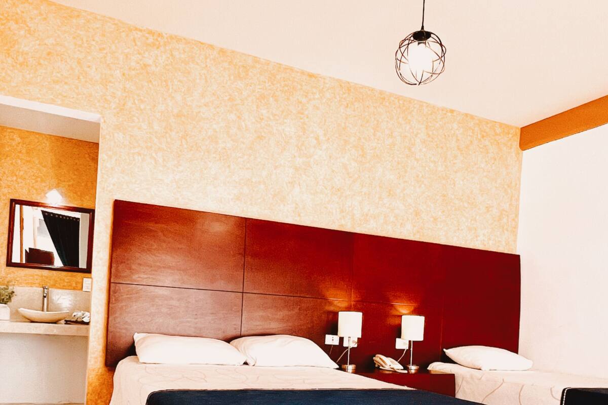 A hotel room with a large bed, a nightstand with two lamps, a mirror, and a red accent wall.