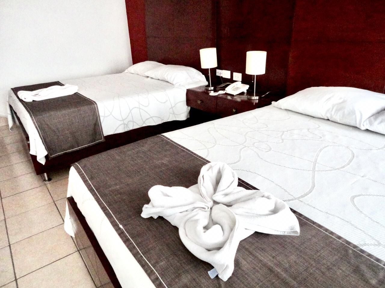 A hotel room with two beds, each with a white comforter and a dark headboard. There are two bedside tables with lamps and a telephone.