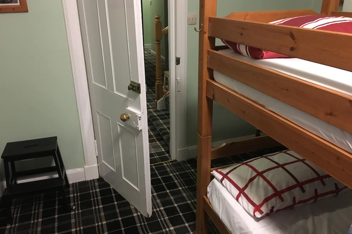 A room with a bunk bed, a door, a small stool, and a checkered floor.