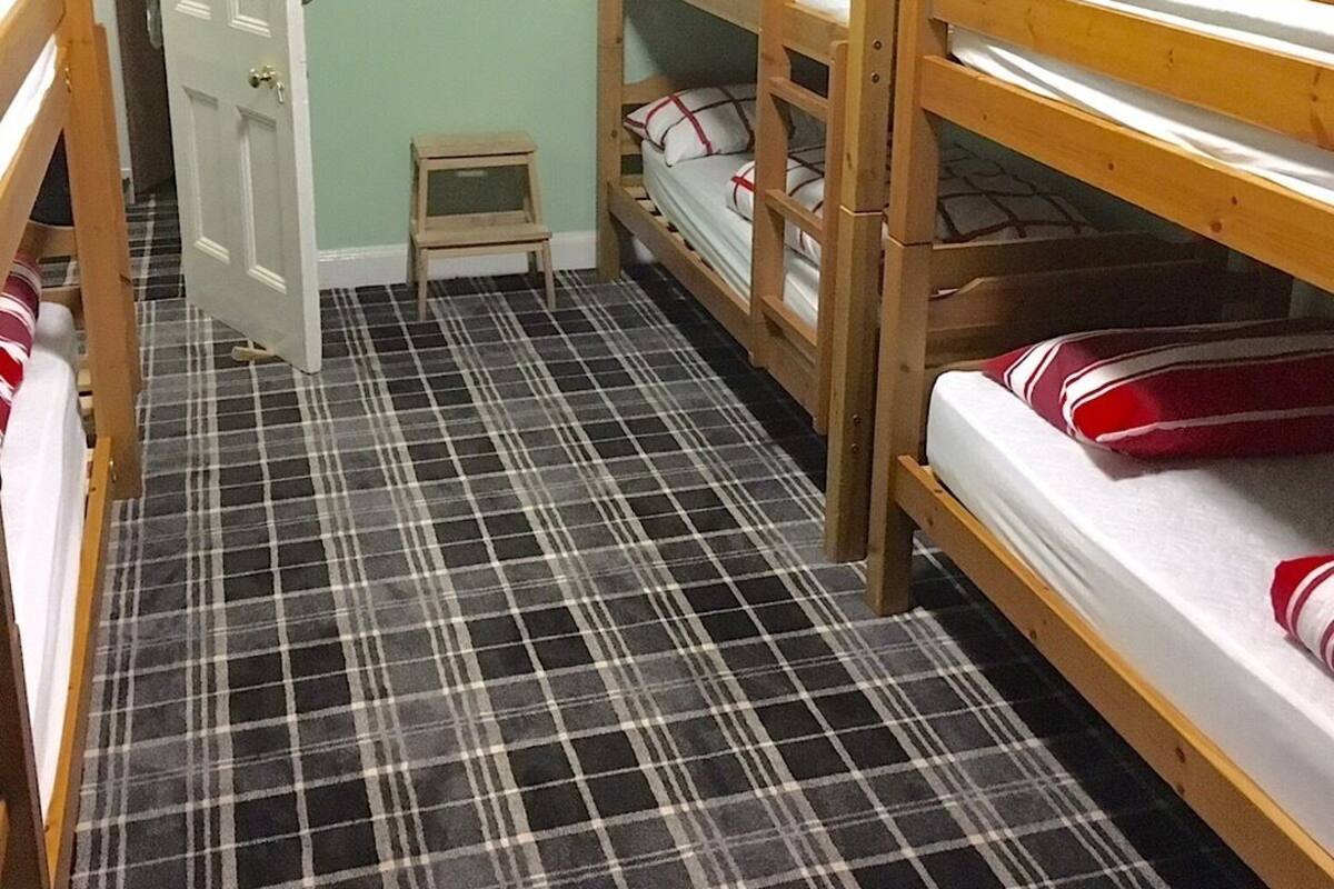 A bunk bed room with a plaid floor, a small wooden stool, and a door leading to another room.