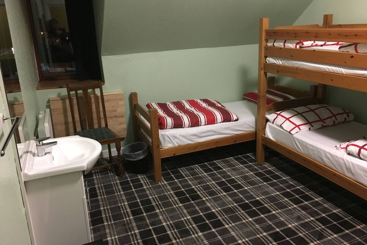 A small, compact room with a bunk bed, a single bed, a chair, a sink, and a mirror.