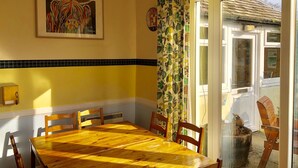 Een eethoek met een houten tafel en stoelen, een schilderij in een lijst aan de muur, en een raam met uitzicht.