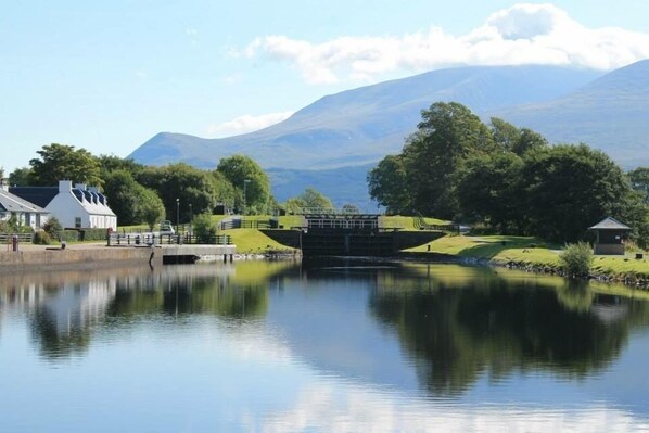 A tranquil riverside scene with a lock gate, a small building, and a mountain in the background.