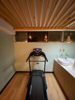 A modern bathroom with a wooden floor, a black treadmill, and a large mirror above the sink.