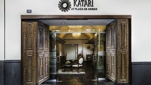 Entrada de un hotel con puertas de madera decoradas y un letrero que dice "KATARI AT PLAZA DE ARMAS".