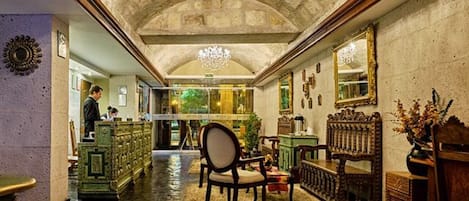 A grand hallway with ornate furniture, a chandelier, and a mirror reflecting the room.