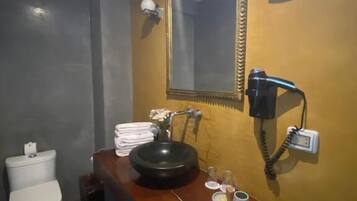 A bathroom with a white toilet, a black sink, and a mirror. There is a towel rack with folded towels and a small table with toiletries.