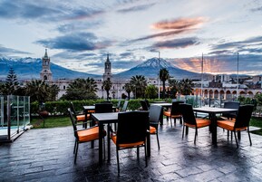 Un espace de restauration en plein air avec des tables et des chaises, une structure vitrée et une vue sur une montagne et une église en arrière-plan.