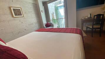 Una habitación de hotel con una cama grande, un escritorio pequeño con una silla, un ventanal con vistas al exterior y un cuadro en la pared.
