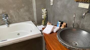 A bathroom with a white bathtub, a stone sink, and a wooden countertop.