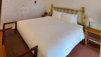 Una cama bien tendida con cabecera dorada, una silla de madera, una mesita de noche con lámpara y una pared decorada.