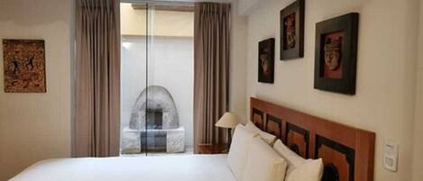 A hotel room with a bed, a stone fireplace, a large window with curtains, and framed pictures on the wall.