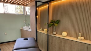 Un moderno cuarto de spa con una camilla de masaje, paneles de madera, un lavamanos y un espejo.
