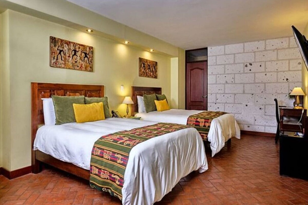 A hotel room with two beds, a brick wall, and artwork on the walls.