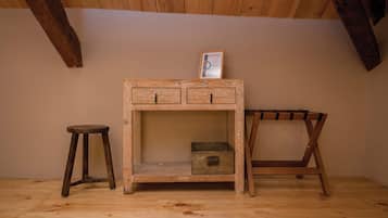 Simple, rustic room with a wooden table and stool, featuring a framed certificate on the wall.