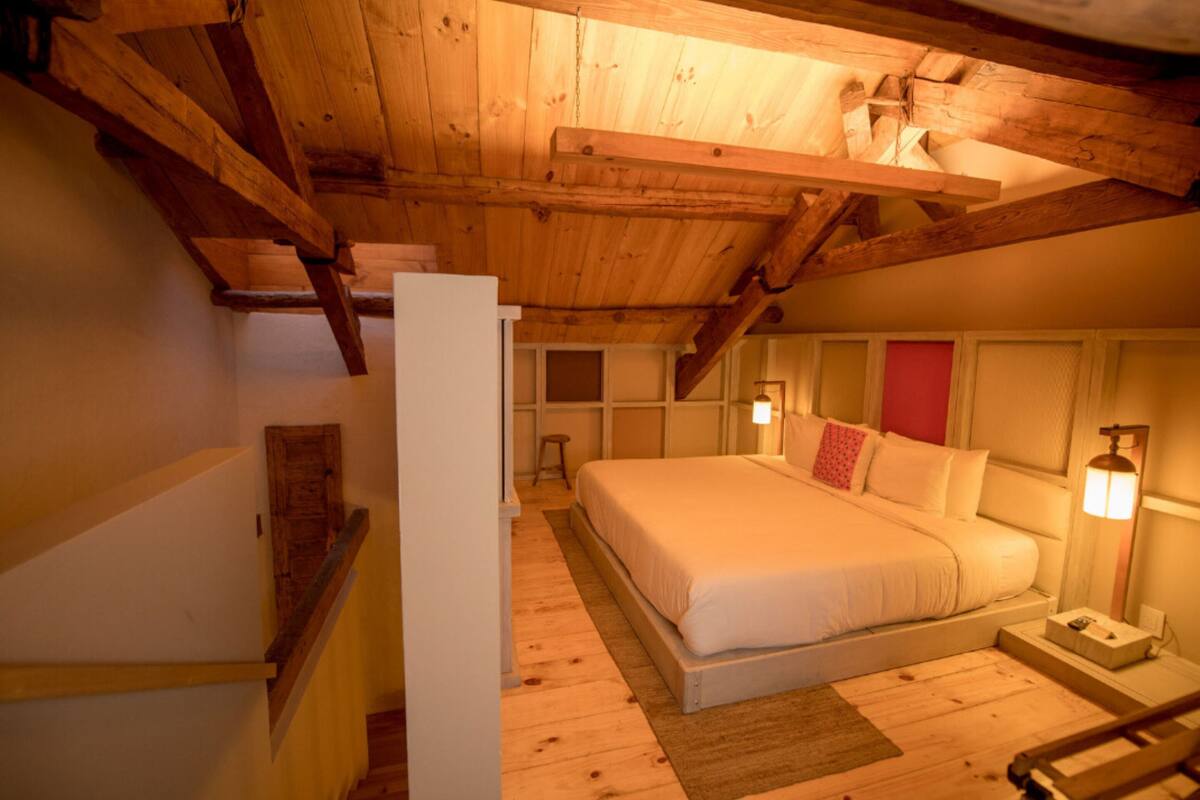 A bedroom with a wooden ceiling, a bed, a nightstand, and a lamp.