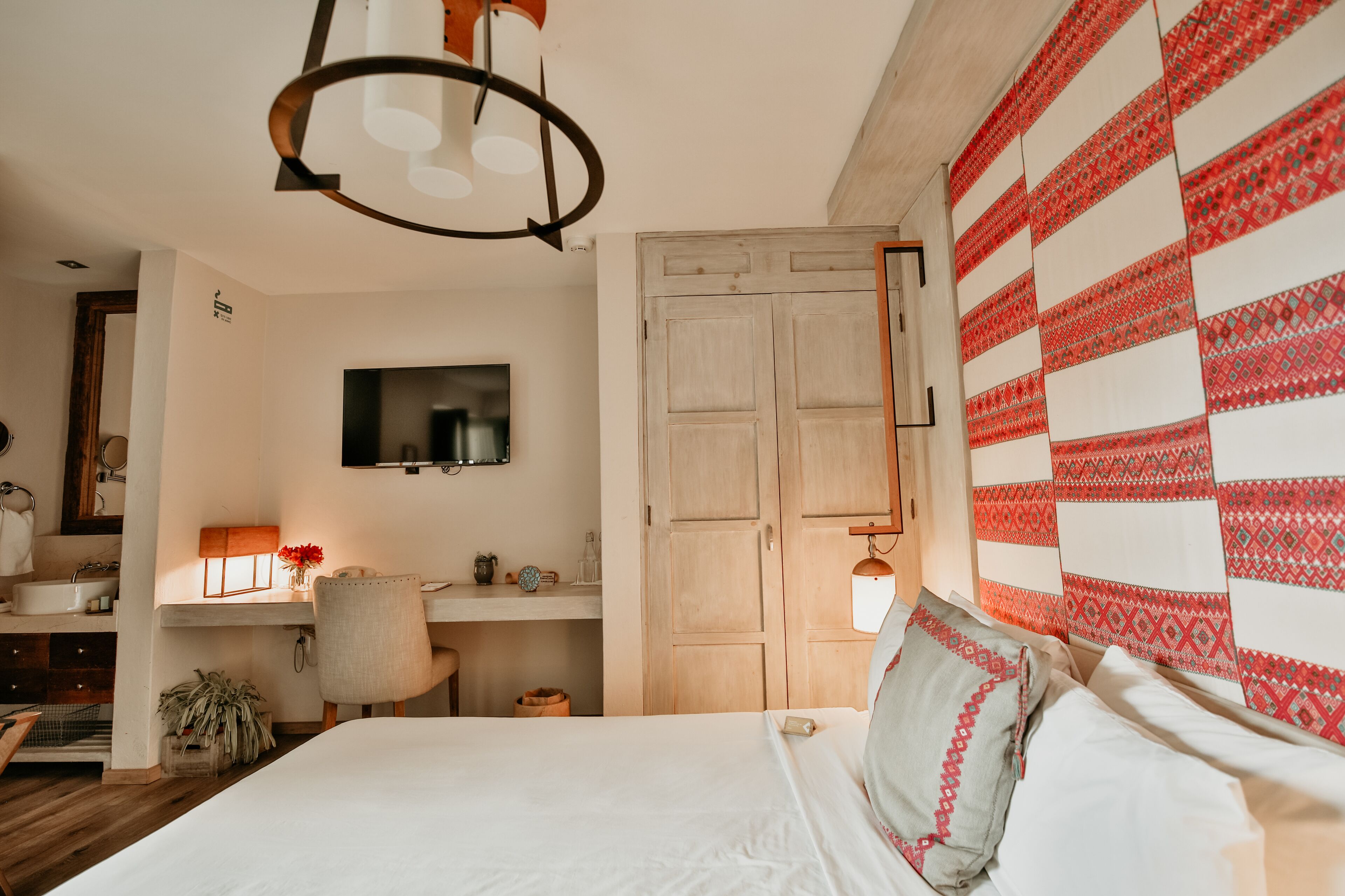 A bedroom with a bed, a desk, a chair, a wardrobe, and a wall-mounted TV.
