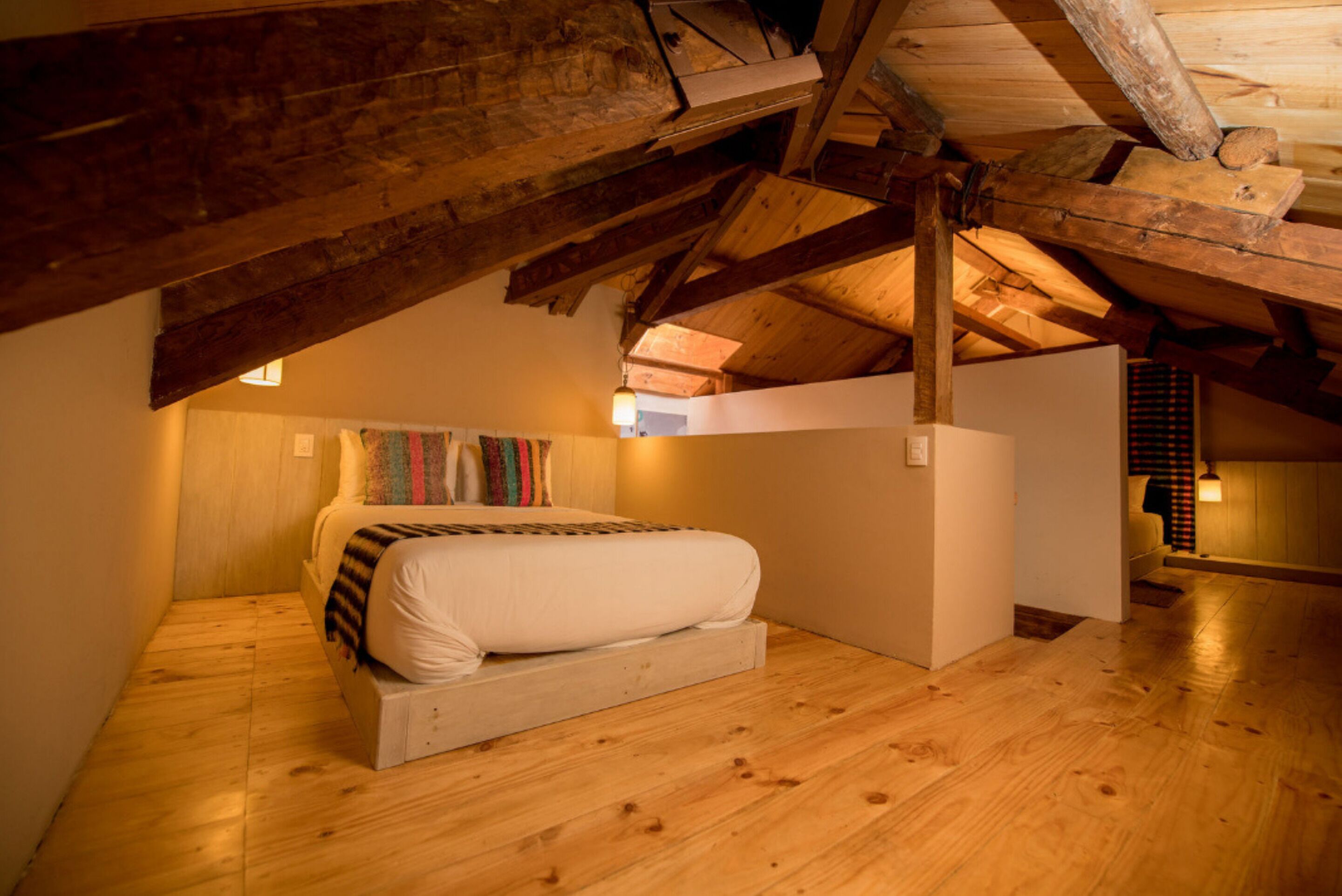 Una camera da letto mansardata accogliente, con soffitto in legno, un letto con coperta a righe e un arazzo colorato.
