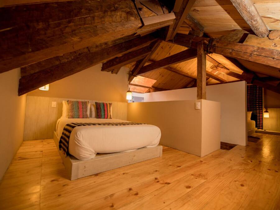 Una camera da letto mansardata accogliente, con soffitto in legno, un letto con coperta a righe e un arazzo colorato.