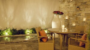 Un patio al aire libre con mobiliario de mimbre, una mesa redonda y un jarrón con flores.