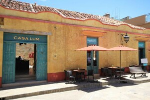 Un bâtiment portant l’enseigne « CASA LUM », doté d’une terrasse avec des parasols et d’un toit recouvert de tuiles.