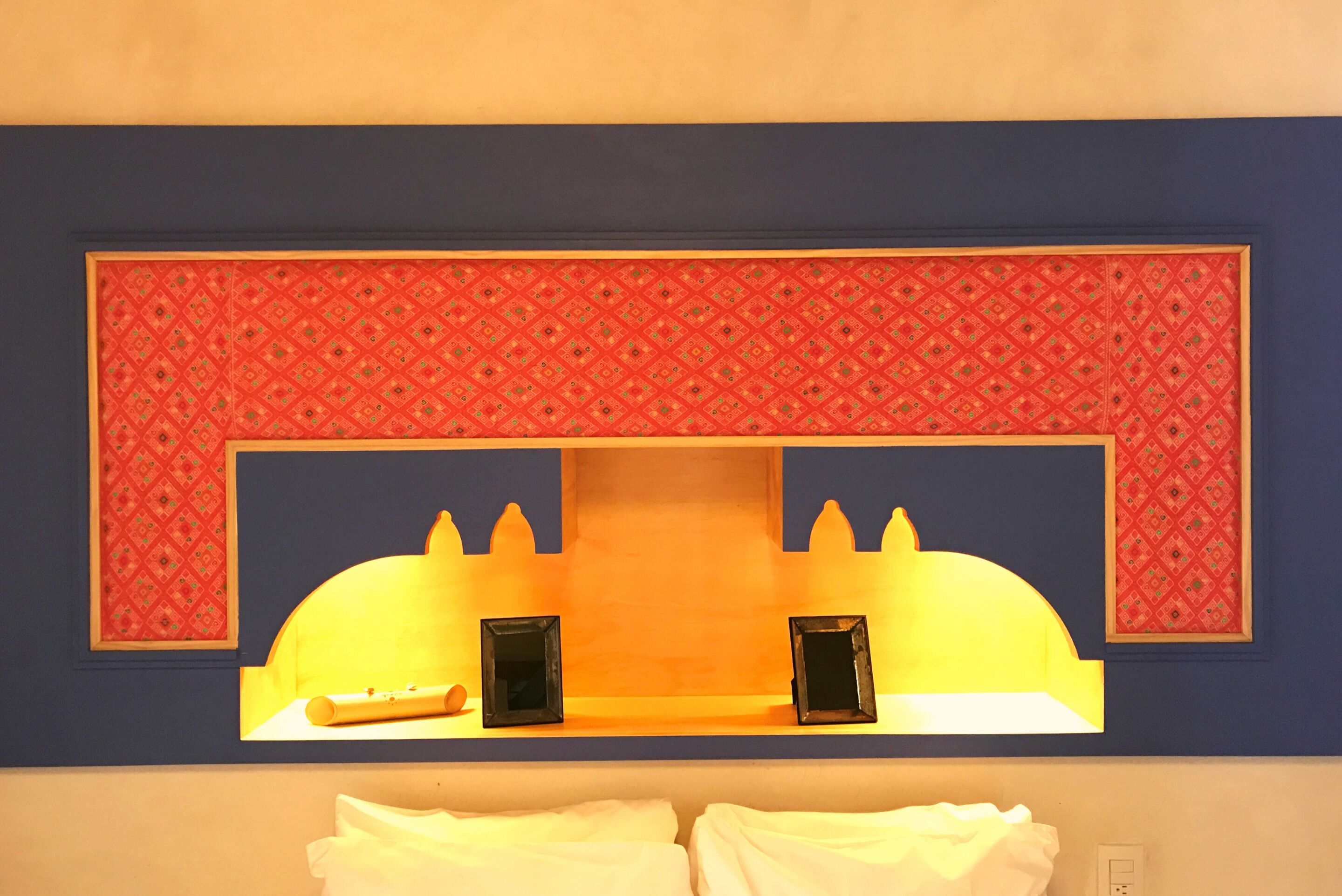 A hotel room with a decorative wall panel, two framed pictures, and a bed with white linens.