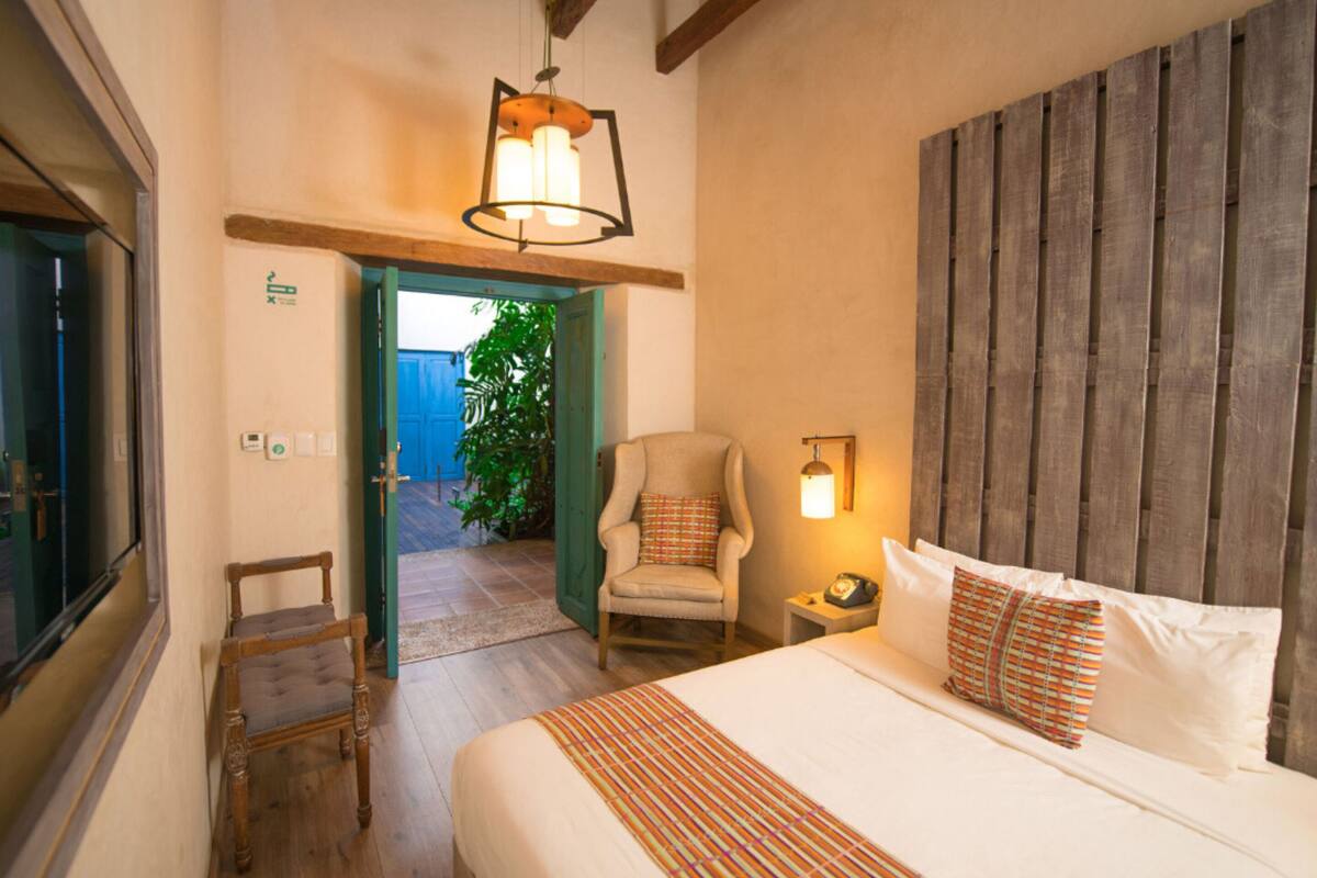 A bedroom with a bed, a chair, a nightstand, a lamp, and a wooden headboard.