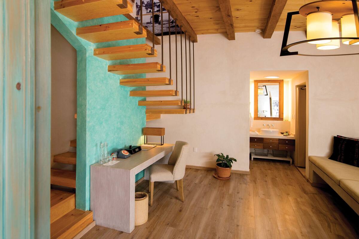 A modern interior with a wooden staircase, a desk with a chair, a potted plant, and a bench.